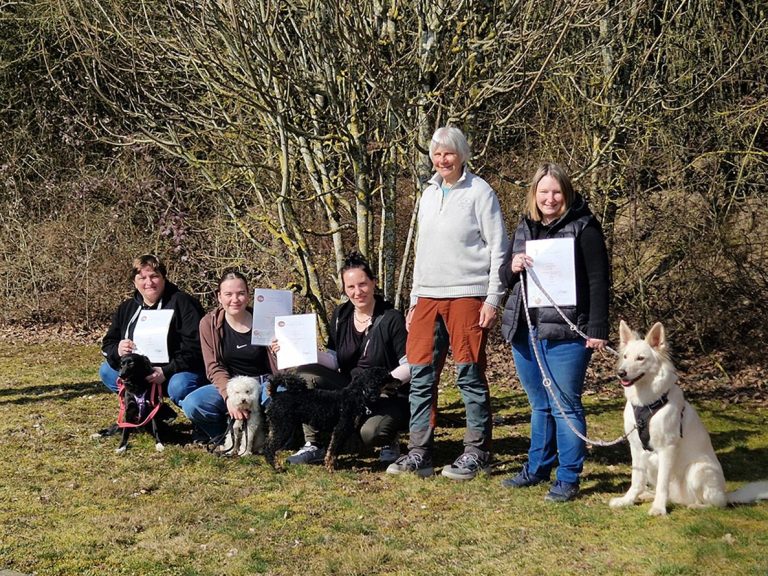 Kurs Hundeführerschein Christiana Gramlich Hundetrainerin Sechs Personen stehen mit Hunden vor einem Baum und halten Unterlagen in der Hand.